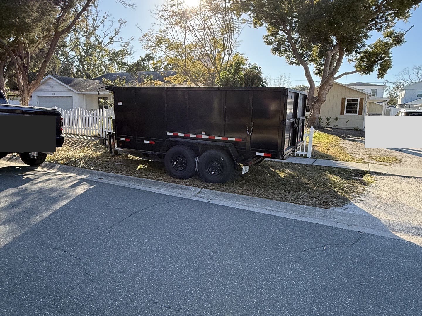Empty 7x14 dump trailer parked on a residential street in St. Petersburg, golden hour sun through trees.